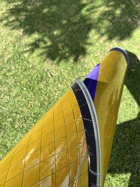 Duotone Duke 5.4 2026 Kiteboard mit gelb-blauem Design und Wabenstruktur, Draufsicht auf grünem Untergrund