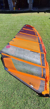 Orange and black Neil Pryde Speedster 6.7 windsurfing sail laid out on green grass with garage in background