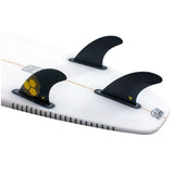 Futures AM2 Alpha Thruster Finnen Set mit drei schwarzen Flossen auf weißem Surfboard, gelbe Wabenstruktur sichtbar