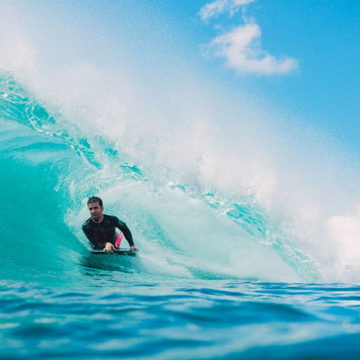 Wave Power Bodyboard Woop in Schwarz und Rosa, Fahrer in türkiser Welle beim Surfen