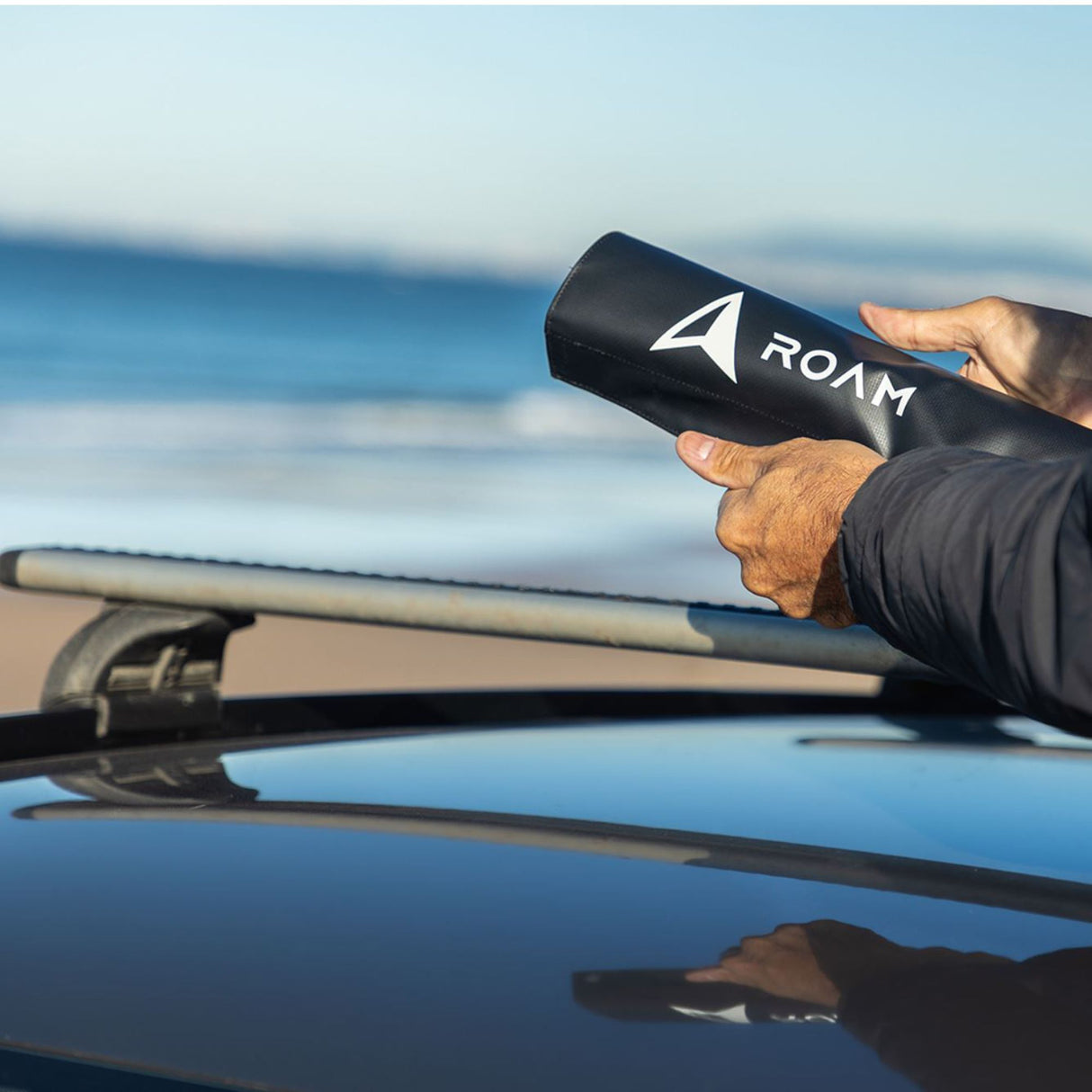 ROAM Dachauflage Surfboard Rund schwarz, runde Schaumstoff-Auflage für Autodächer, in Hand gehalten am Strand