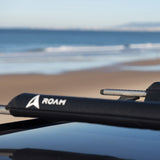 ROAM Dachauflage Surfboard Flach schwarz auf Autodach, Strandszene im Hintergrund