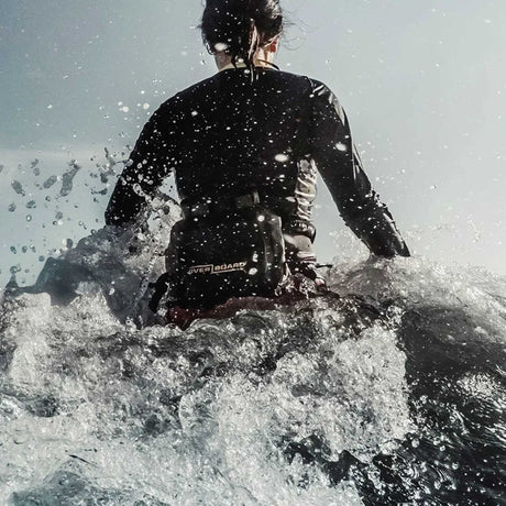 OverBoard wasserdichte Hüfttasche LIGHT in Schwarz, getragen bei Wassersport, von hinten in Wellen