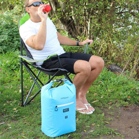 OverBoard Soft Cooler Bag Kühltasche in Hellblau, wasserdicht, neben Campingstuhl im Freien positioniert