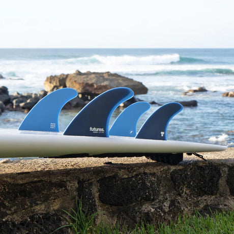 Futures Twiggy Big Wave 5-Fin Set, vier blaue und schwarze Surfflossen aus Kunststoff auf weißem Surfboard-Rail am Strand