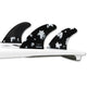 Futures Thruster Fin Set Ando Blackstix, drei schwarze Flossen mit weißem Blumenmuster auf weißem Surfboard, Draufsicht
