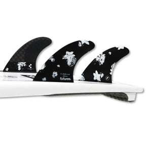Futures Thruster Fin Set Ando Blackstix, drei schwarze Flossen mit weißem Blumenmuster auf weißem Surfboard, Draufsicht