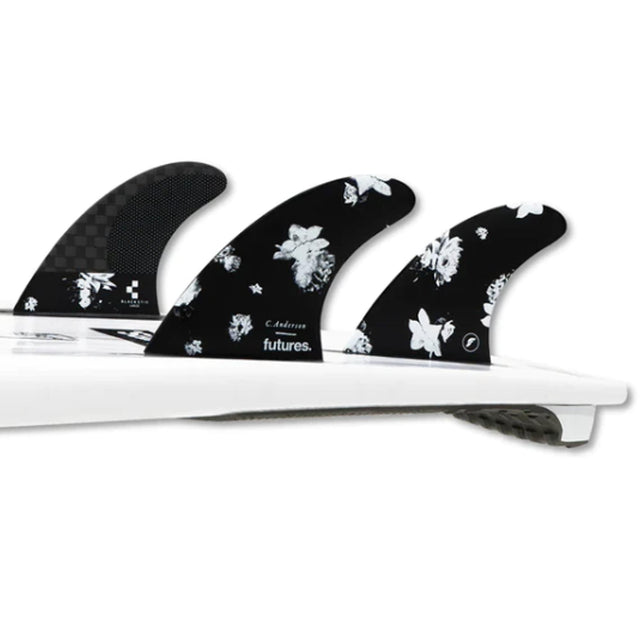Futures Thruster Fin Set Ando Blackstix, drei schwarze Flossen mit weißem Blumenmuster auf weißem Surfboard, Draufsicht