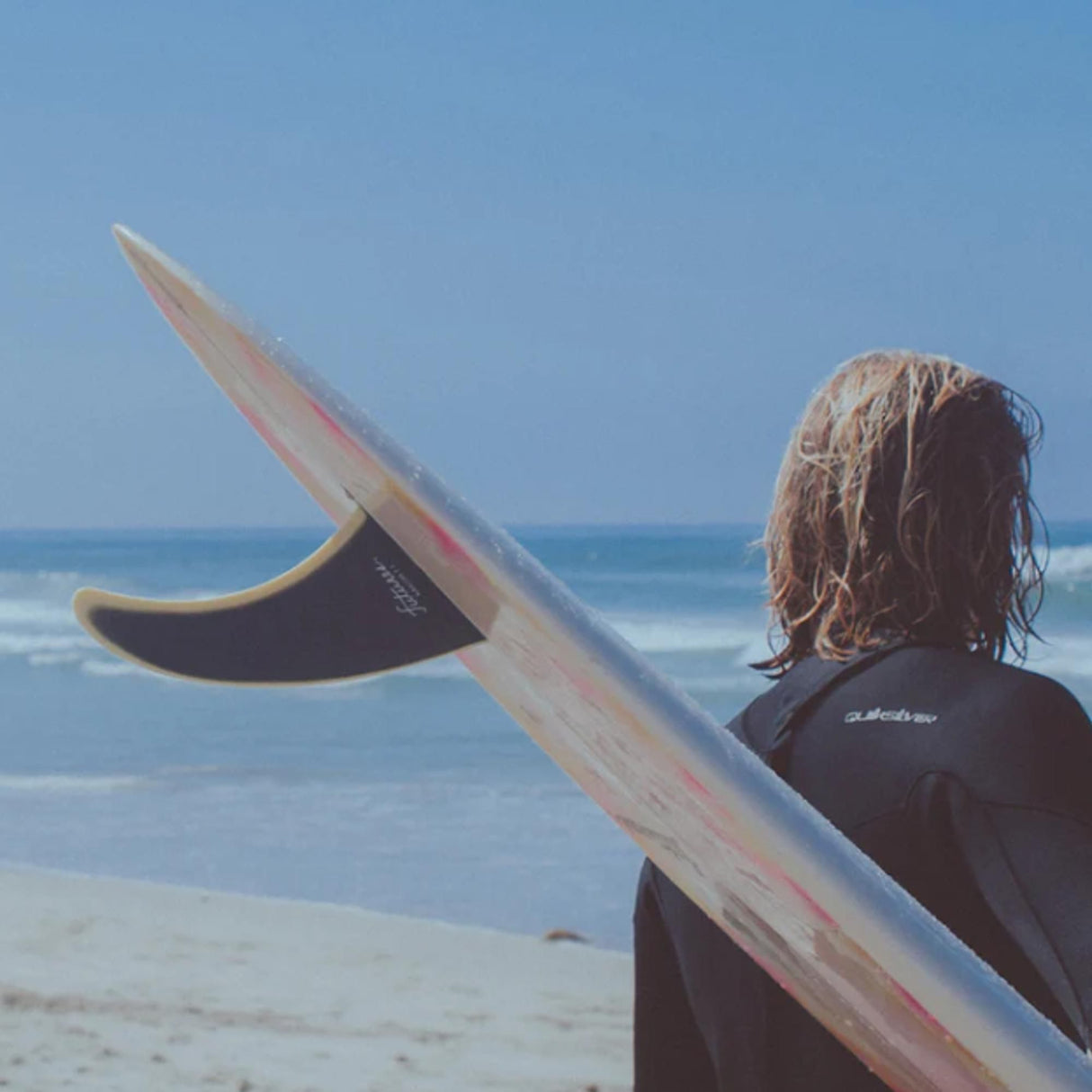 Futures Single Fin Albacore Flex Fiberglass, beige-rosé, Surfer trägt Flosse am Strand mit Meeresblick