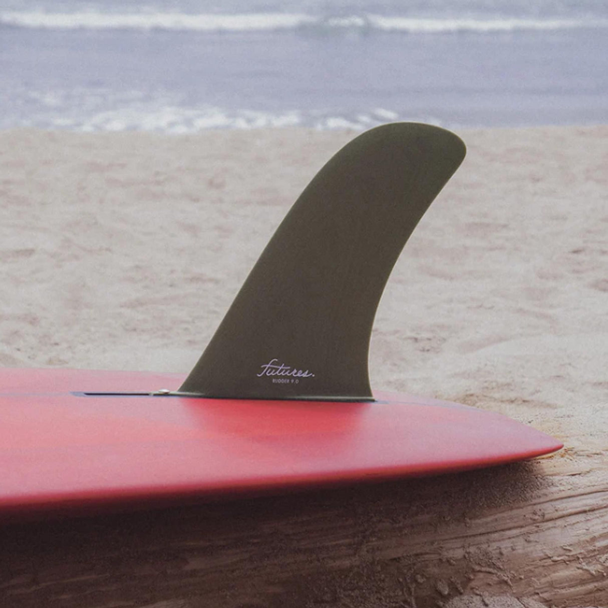 Futures Single Fin Rudder Fiberglass US, schwarze Finne auf rosa Surfboard am Strand