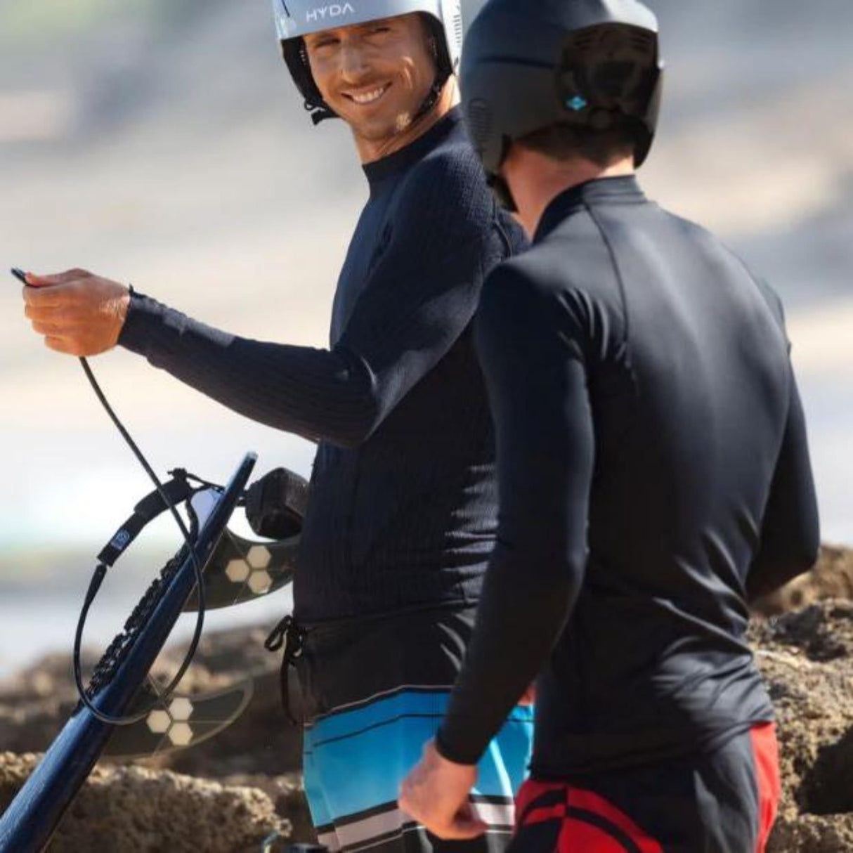 HYDA Coanda Core Wassersport Helm in Weiß und Schwarz, getragen von zwei Wassersportlern mit Kiteboard am Strand
