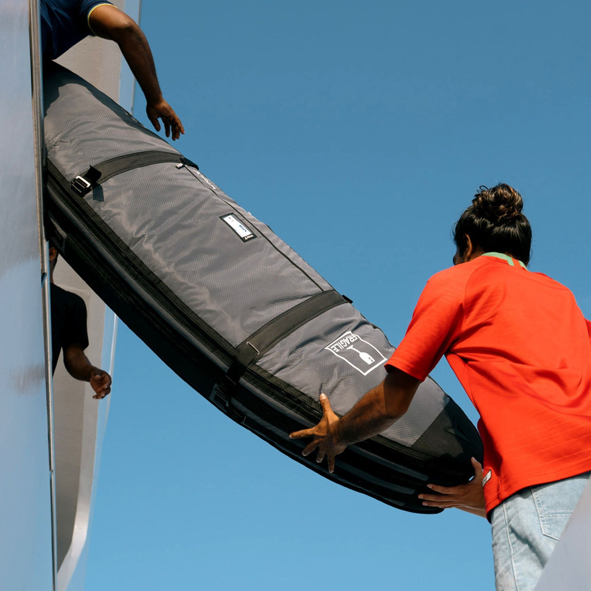 Roam Surfboard Converter Coffin Tasche grau-schwarz, zwei Personen laden Surfboard, Transporttasche mit Griffen