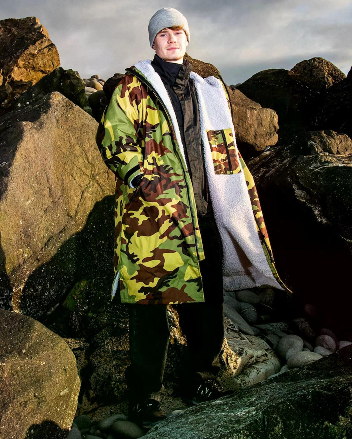 Dryrobe Advance Long Sleeve in Camouflage und Weiß, getragen von Person zwischen Felsen, Frontalansicht