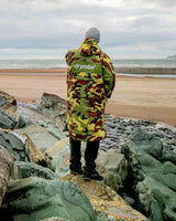 Dryrobe Advance Long Sleeve in Neon Gelb-Rot Camouflage, getragen am Strand, Rückansicht auf Steinen