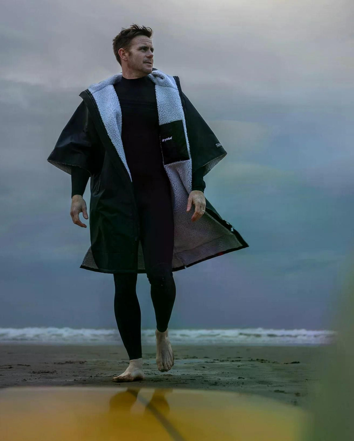 DRYROBE Advance Kurzarm in Schwarz mit hellblauem Fleece-Futter, Mann am Strand tragend