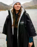 DRYROBE Advance Kurzarm schwarzer Umhang mit Sherpa-Futter, Frontansicht an einem See getragen