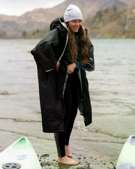 DRYROBE Advance Kurzarm in Schwarz, Frau am Strand mit Surfboards, Funktionsmaterial, Übergangsjacke