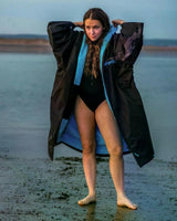 DRYROBE Advance Kurzarm in Schwarz mit blauem Innenfutter, Frau am Strand trägt offenen Bademantel