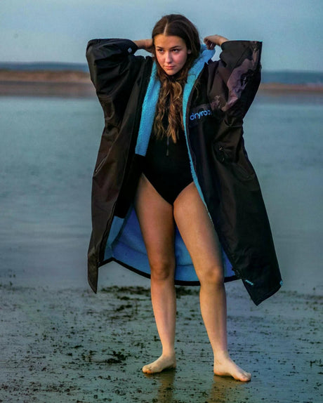 DRYROBE Advance Kurzarm in Schwarz mit blauem Innenfutter, Frau am Strand trägt offenen Bademantel
