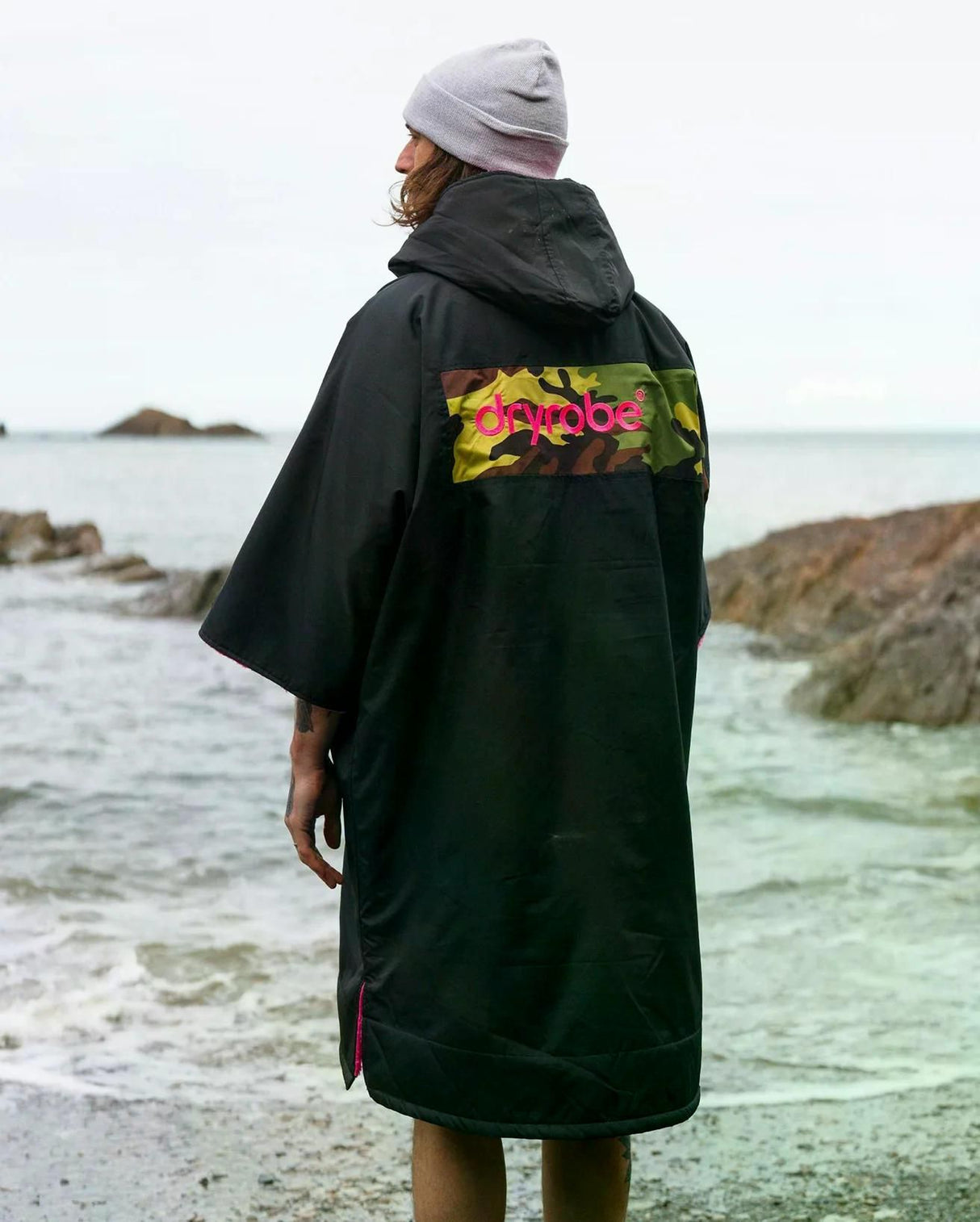 DRYROBE Advance Kurzarm Umhang in Schwarz mit farbigem Rückendruck, getragen am Strand, Rückansicht