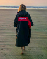 DRYROBE Advance Short Sleeve Umhang in Schwarz und Rot, getragen am Strand, Rückansicht