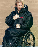 Dryrobe Adapt Mantel schwarze Funktionsjacke mit Kapuze, getragen im Rollstuhl sitzend, Frontansicht