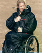 Dryrobe Adapt Mantel schwarze Funktionsjacke mit Kapuze, getragen im Rollstuhl sitzend, Frontansicht