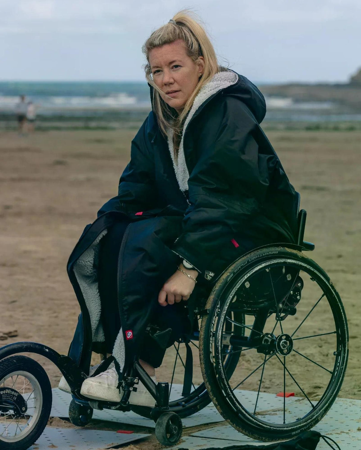 Dryrobe Adapt Mantel in Dunkelblau mit Fleece-Futter, getragen von Frau im Rollstuhl am Strand