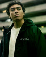 Dryrobe Nexus Long Sleeve dunkelgrün mit Kapuze, Frontansicht auf Person getragen, Reißverschluss und Dryrobe-Logo sichtbar