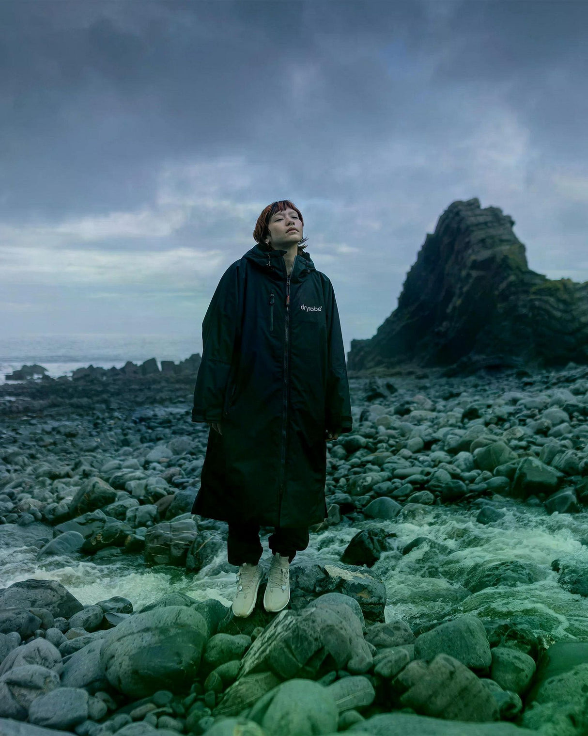 Dryrobe Nexus Long Sleeve schwarzer Umhang mit Kapuze, getragen am Strand, Frontalansicht