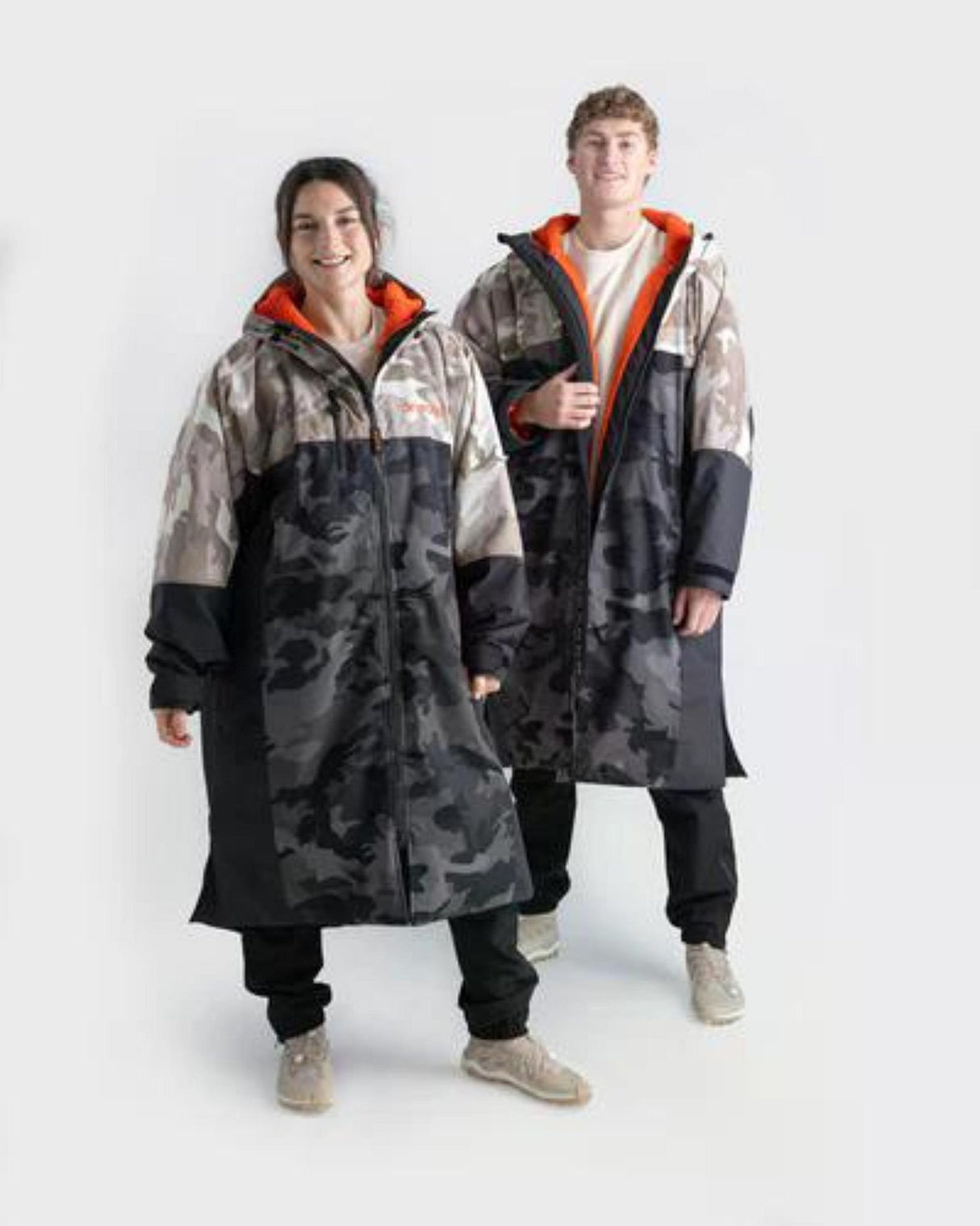 Dryrobe Nexus Long Sleeve Umhang in Schwarz und Grau mit orangerotem Kragen, getragen von zwei Personen in Frontalansicht