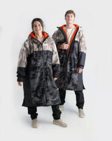 Dryrobe Nexus Long Sleeve Umhang in Schwarz-Grau mit roten Innenfutter, zwei Personen tragend, Frontalansicht