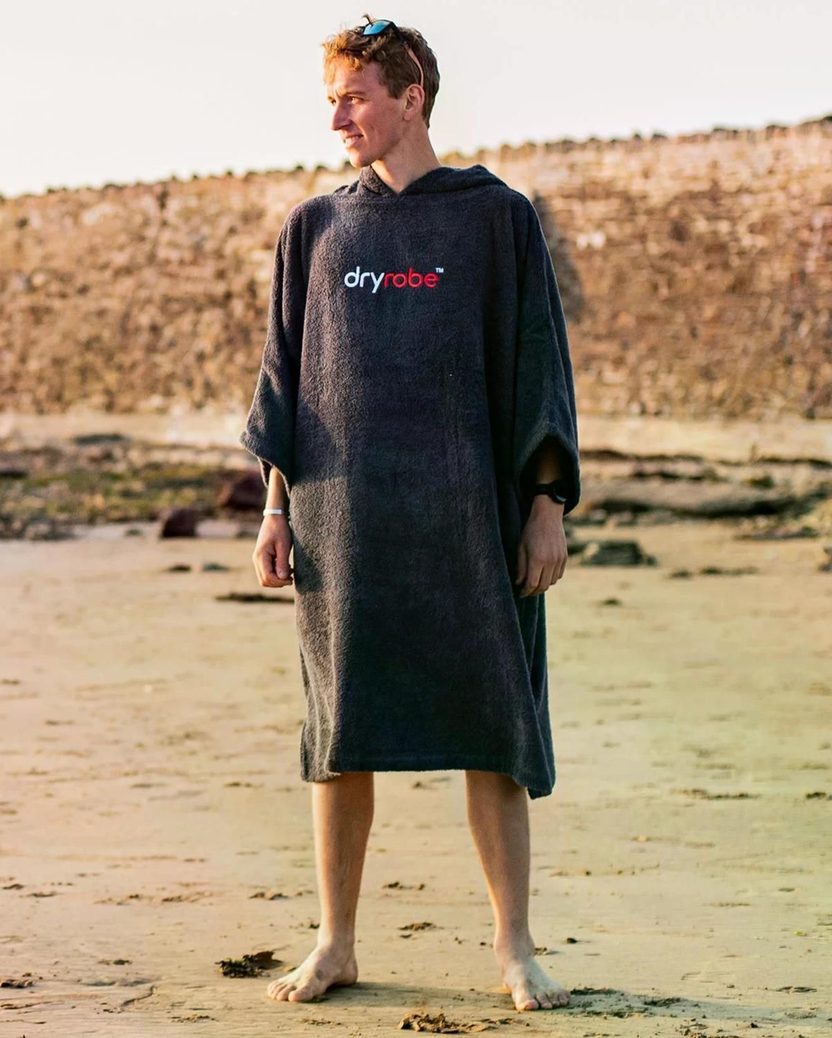 Dryrobe Handtuchmantel aus Bio-Baumwolle in Dunkelgrau, getragen am Strand, mit Kapuze und Logo-Print