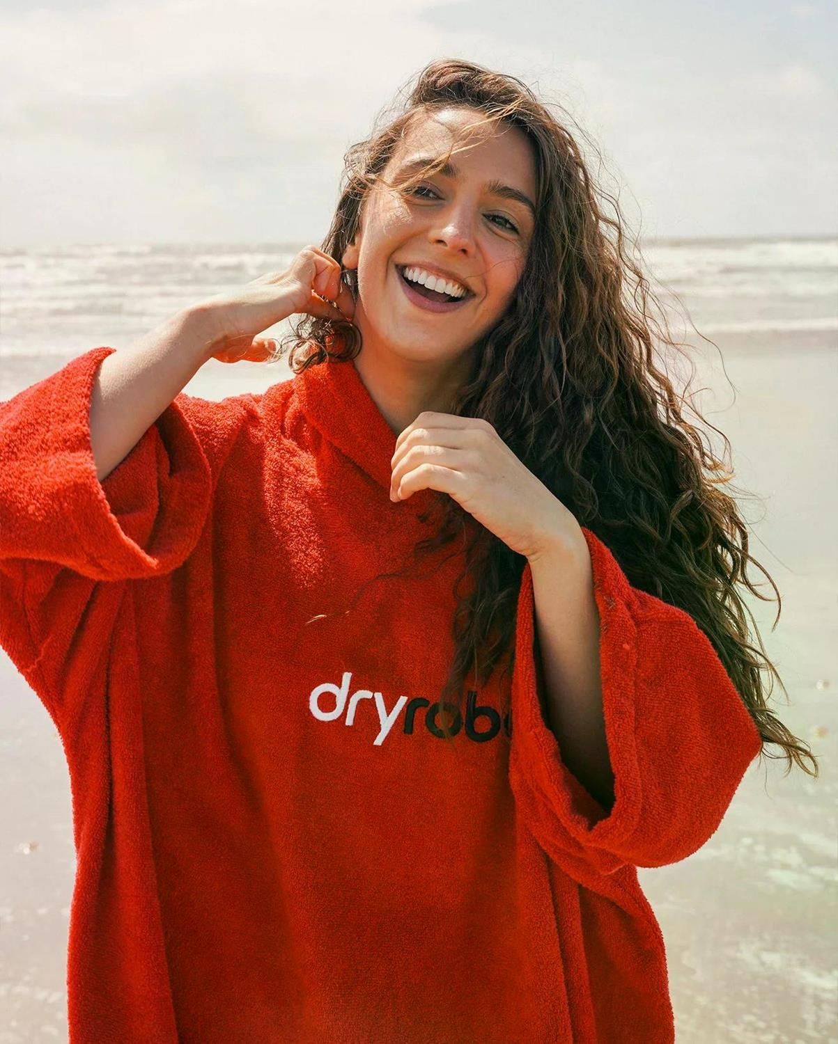 Dryrobe Handtuchmantel Bio-Baumwolle in Rot, getragen am Strand, mit weißem Logo