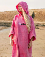 Dryrobe Handtuchmantel aus Bio-Baumwolle in Pink, mit Kapuze, Frontansicht am Strand getragen