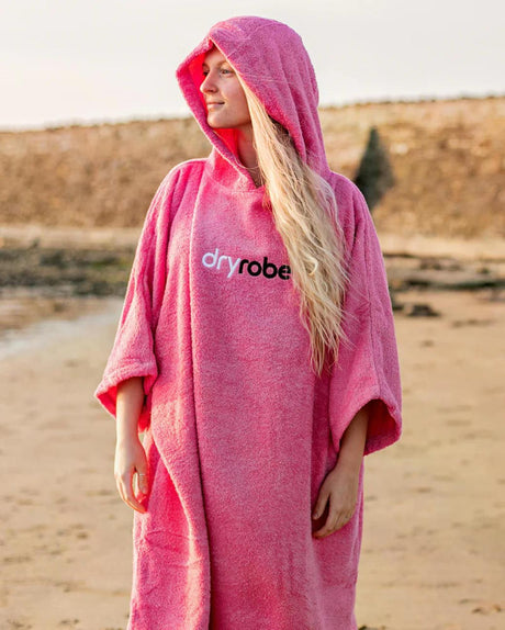 Dryrobe Handtuchmantel aus Bio-Baumwolle in Pink, mit Kapuze, Frontansicht am Strand getragen