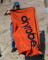 Dryrobe Strandtuch in Orange mit schwarzem Logo, von Person am Strand gehalten