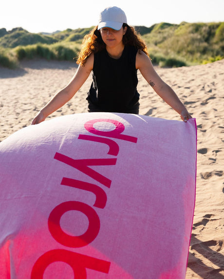 Dryrobe Strandtuch in Rosa mit Dryrobe-Logo, Frau hält Handtuch am Strand, Frontansicht