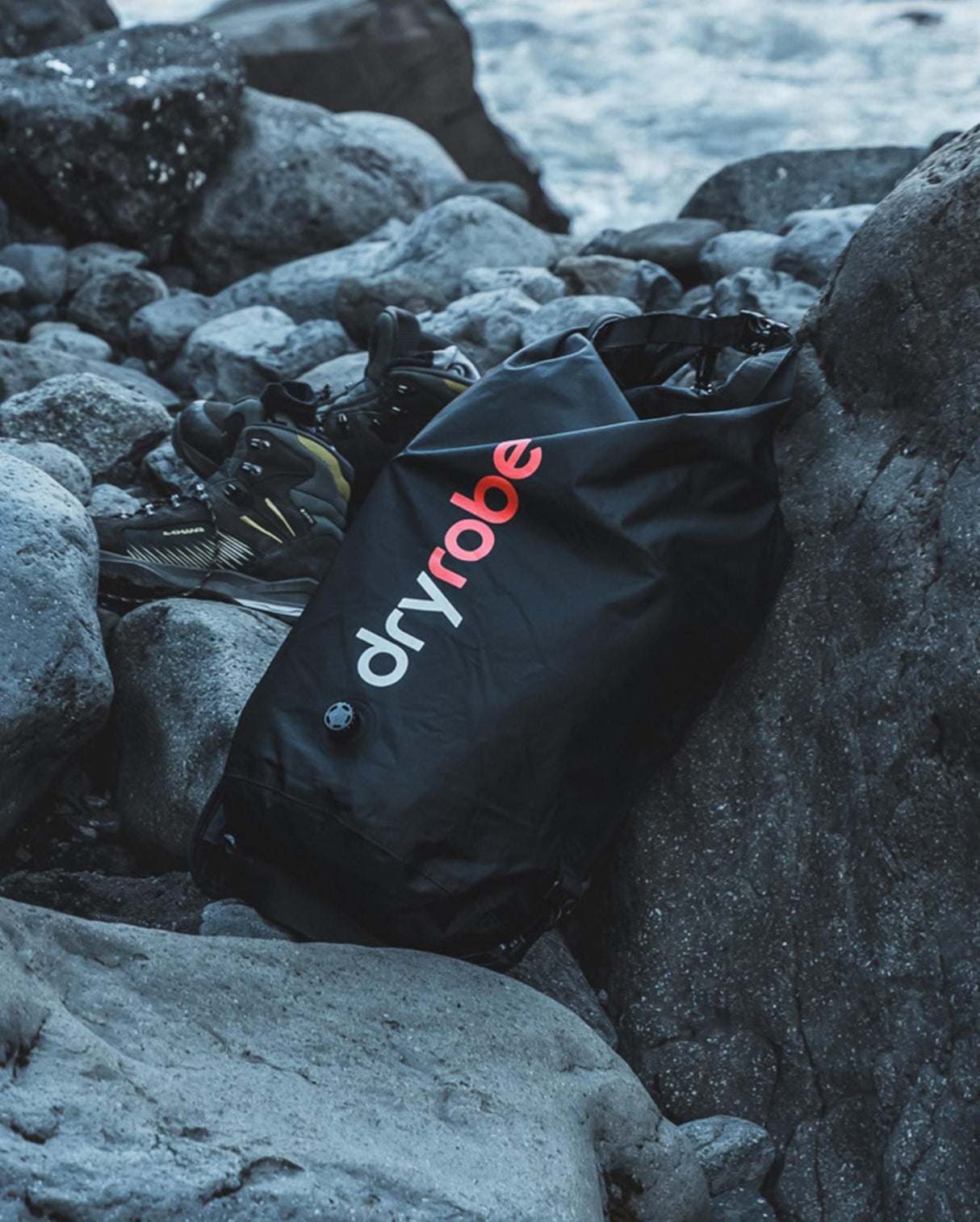 Dryrobe schwarzer wasserdichter Packsack zwischen Felsen am Strand, wasserfestes Material mit rotem Logo