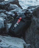Dryrobe schwarzer wasserdichter Packsack zwischen Felsen am Strand, wasserfestes Material mit rotem Logo
