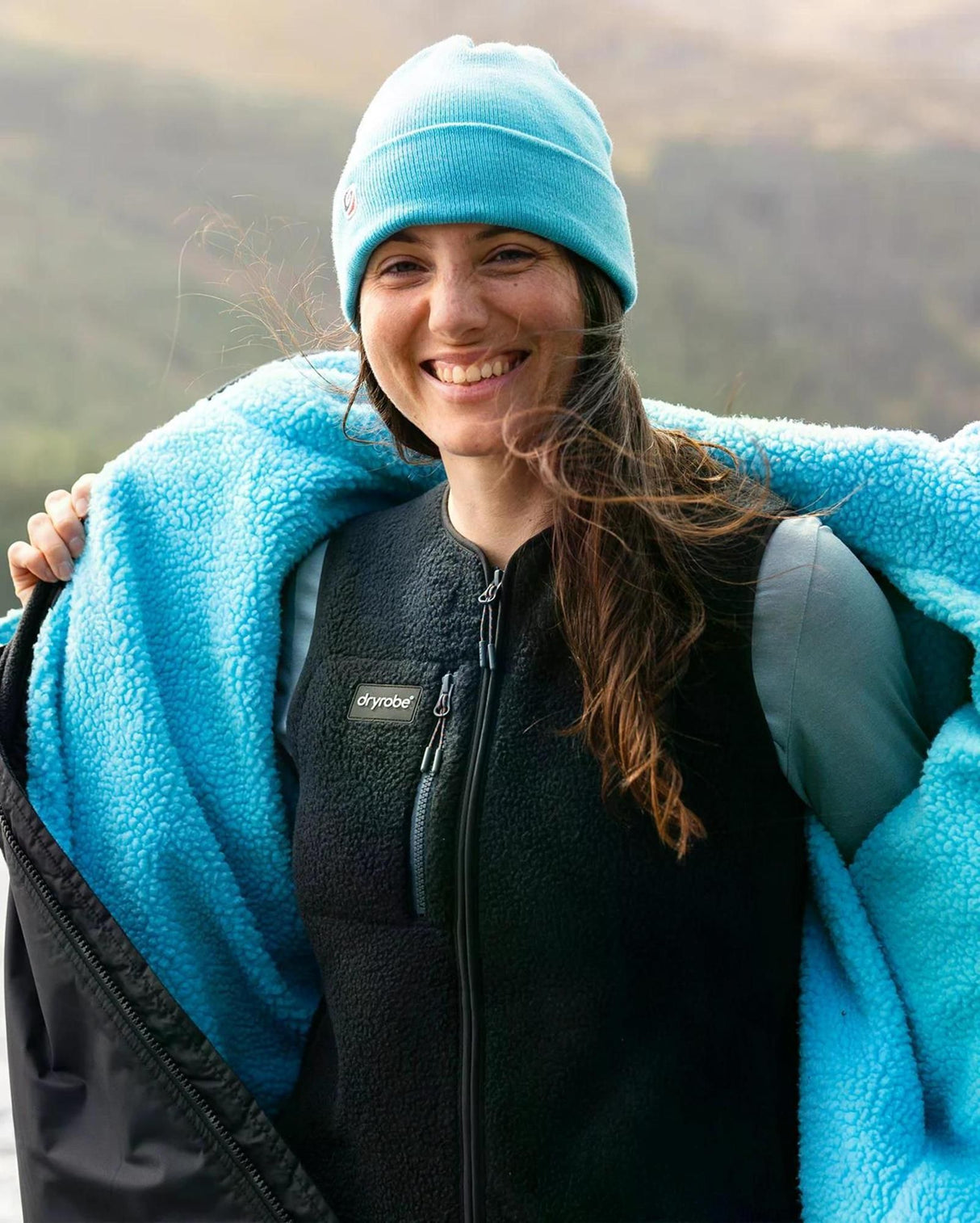 Dryrobe Thermo Weste in Schwarz und Blau, Frau trägt Weste über schwarzer Fleece-Jacke, Vorderansicht