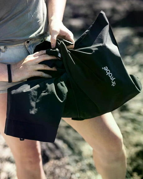 Dryrobe Tech-Lite Kurzarm in Schwarz, kompaktes Handtuch-Design, wird von Person gehalten, leichte Materialstruktur sichtbar