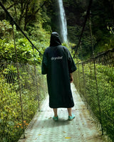 Dryrobe Tech-Lite Kurzarm in Schwarz, Rückenansicht, Person trägt Umhang in grüner Natur