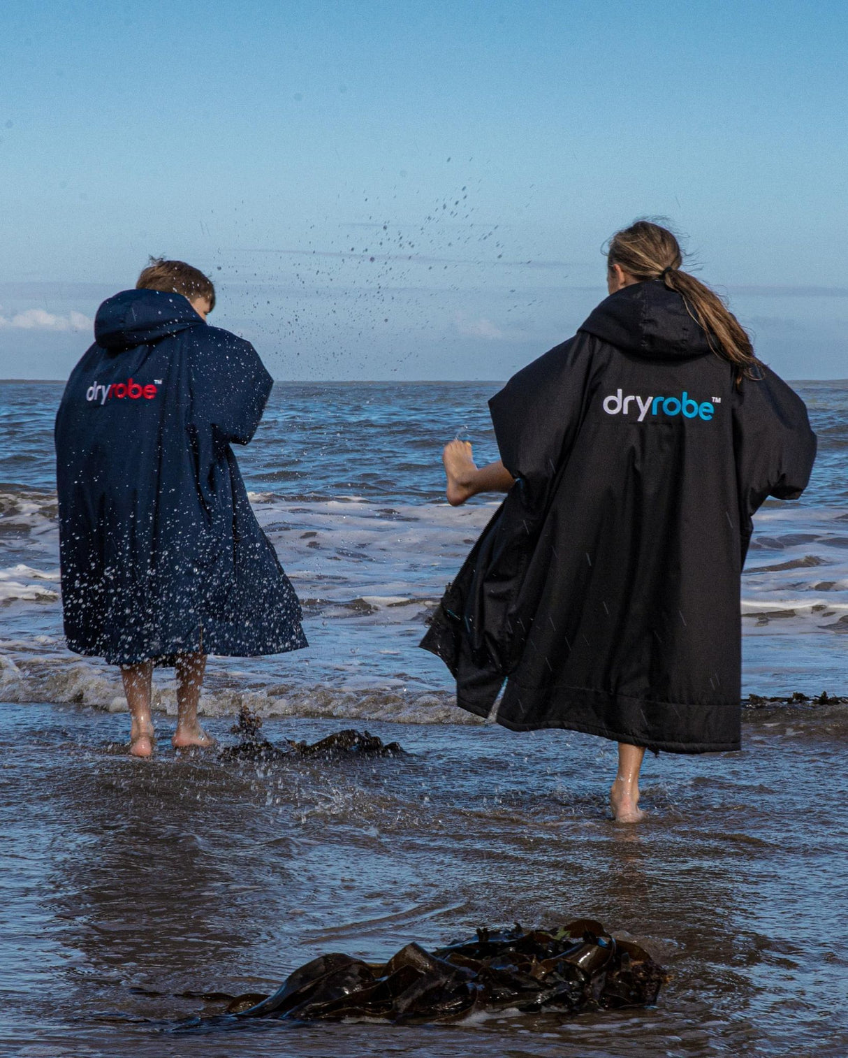 Dryrobe Advance Langarm Kinder in Marineblau und Schwarz, wasserdichte Umziehjacke aus Neopren, zwei Kinder am Strand im Meer