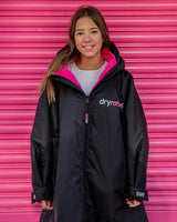 Dryrobe Advance Long Sleeve Kids Jacke in Schwarz mit Neonpink, Frontalansicht auf Mädchen mit Kapuze