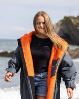 Dryrobe Advance Long Sleeve Kids in Schwarz mit orangefarbenem Fleece-Futter, Frontansicht am Strand getragen