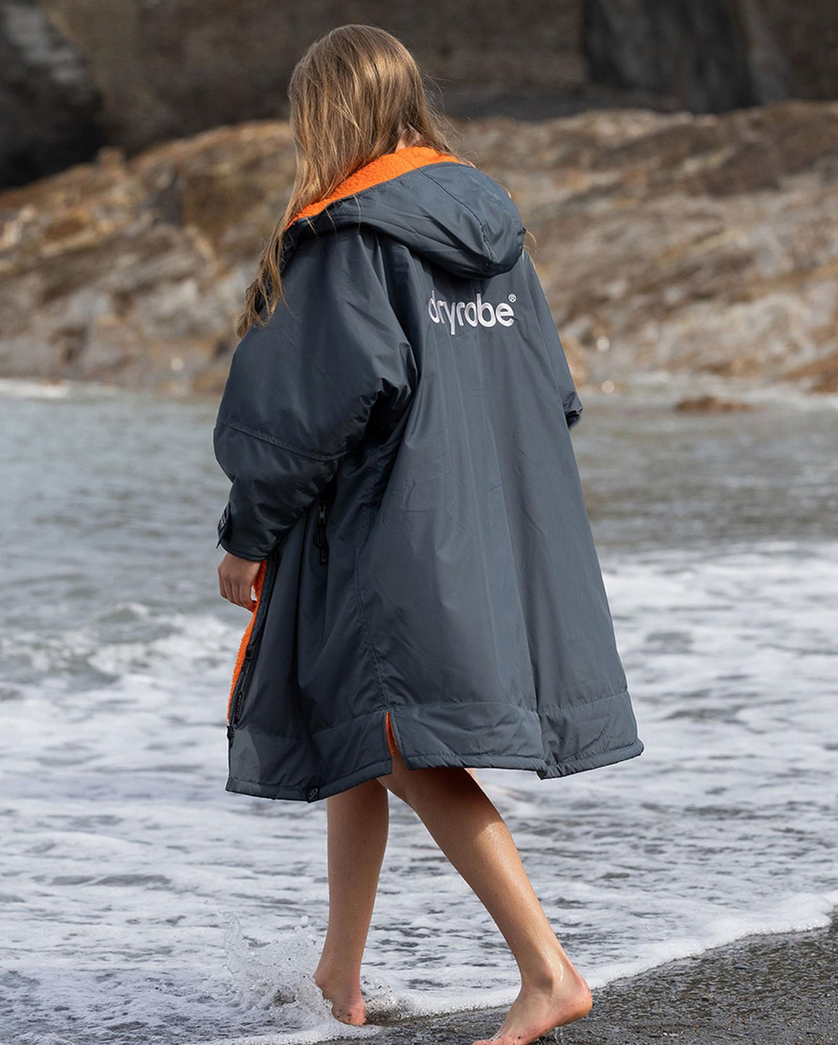 Dryrobe Advance Langarm Kinder in Dunkelblau mit orangem Kragen, getragen am Strand, Rückansicht