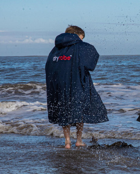 Dryrobe Advance Long Sleeve Kids Bademantel in Marineblau, wasserabweisend, Kind am Strand von hinten