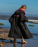 Dryrobe Advance Short Sleeve Kids Umhang in Schwarz und Pink, Mädchen am Strand tragend, Rückansicht