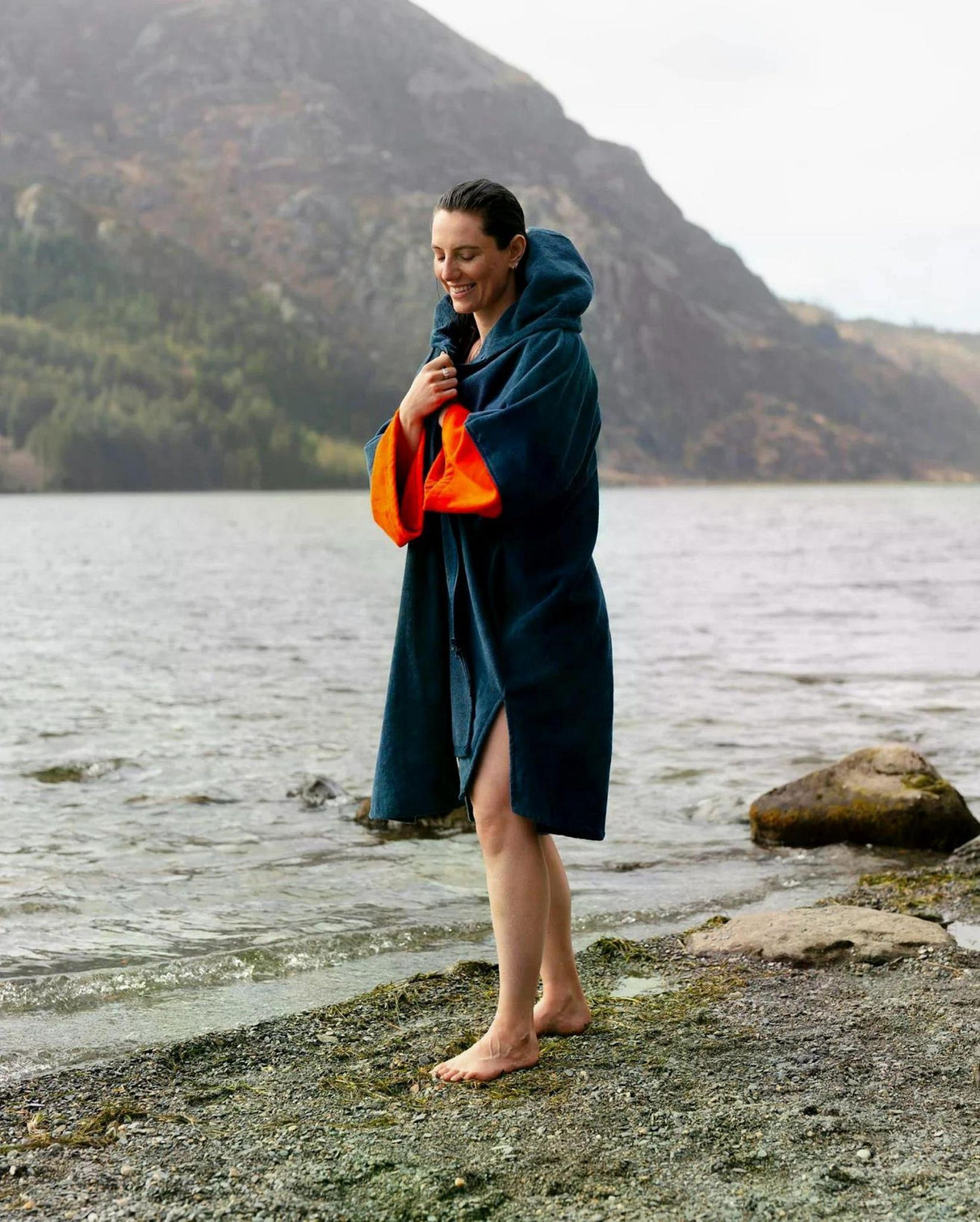 Dryrobe Fullzip Handtuchmantel aus Bio-Baumwolle in Dunkelblau, getragen am See, mit oranger Innenseite sichtbar